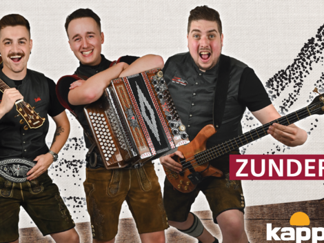 Drei fröhliche Musiker in traditioneller Tracht stehen zusammen. Sie halten verschiedene Instrumente und lächeln in die Kamera.