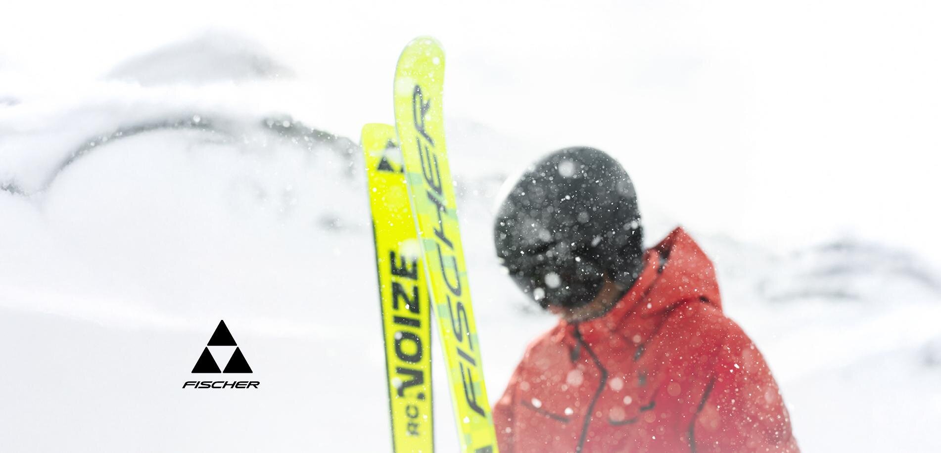 Ein Skifahrer in einem roten Anzug steht im Schnee. Die Umgebung ist winterlich und verschneit, während die Skier leuchtend gelb sind.