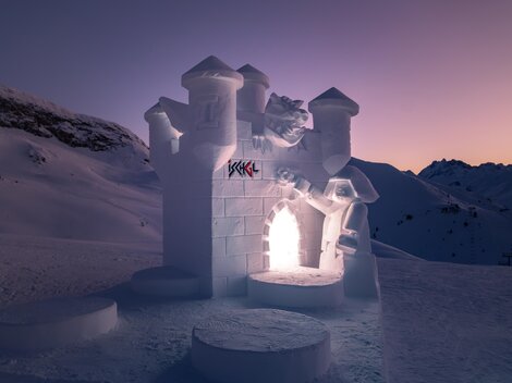 Ein eindrucksvolles Schneeburgenkunstwerk in einer verschneiten Landschaft. Die Burg leuchtet sanft im Dämmerlicht.