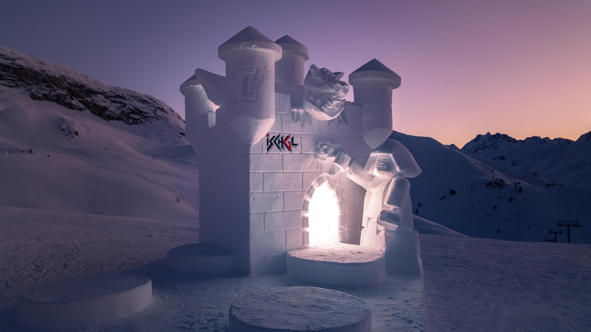 Ein eindrucksvolles Schneeburgenkunstwerk in einer verschneiten Landschaft. Die Burg leuchtet sanft im Dämmerlicht.
