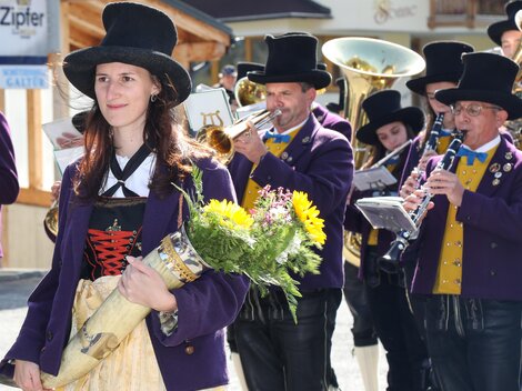 Eine Gruppe von Menschen in traditionellen Trachten marchiert durch die Stadt. Eine Frau hält einen Strauß Blumen in der Hand.