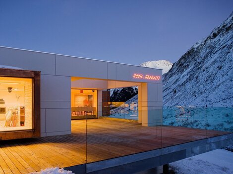 Ein modernes Haus in den Bergen, umgeben von Schnee. Der Balkon bietet einen herrlichen Blick auf die umliegenden Berge.
