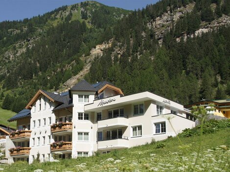Ein modernes Gebäude in den Bergen. Im Hintergrund sind grüne Hänge und Bäume zu sehen.