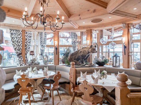 Ein gemütliches Restaurant mit Holzdekor und einer Bärenfigur im Hintergrund. Die Tische sind hübsch gedeckt und schaffen eine einladende Atmosphäre.