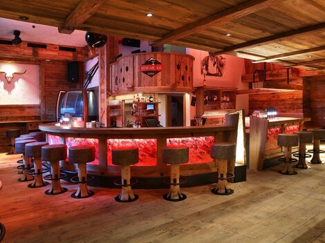 Eine gemütliche Bar mit Holzverkleidung und runden Hockern. Die Beleuchtung sorgt für eine einladende Atmosphäre.