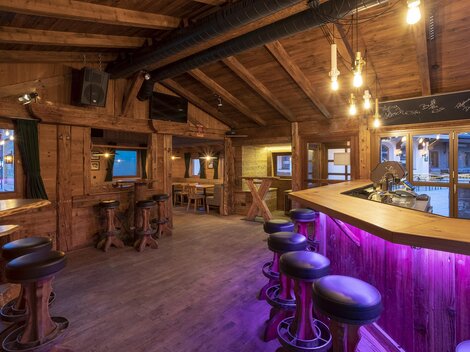 Ein gemütlicher Barbereich mit Holzinterieur und sanfter Beleuchtung. Die Bar hat eine moderne, lila beleuchtete Fläche und einige Sitzgelegenheiten.