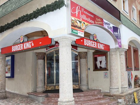 Ein Burger King Restaurant mit auffälligem roten Schild. Das Gebäude hat Säulen und ist in einer urbanen Umgebung.