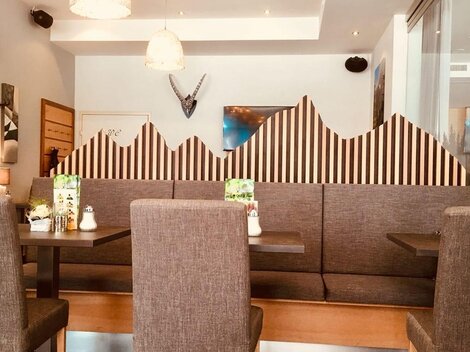Ein modernes Restaurant mit gemütlichen Sitzecken und einer dekorativen Wand im Bergdesign. Das Licht ist hell und freundlich, was eine einladende Atmosphäre schafft.