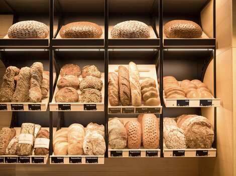 Eine Auswahl an frischem Brot in verschiedenen Formen und Farben. Die Brote sind ordentlich in Regalen angeordnet.