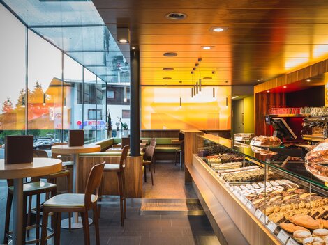 Ein modernes Café mit einer großen Auslage voller Kuchen und Gebäck. Helle Farben und viel natürliches Licht schaffen eine einladende Atmosphäre.