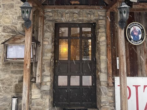 Ein traditionelles Restaurant mit einem holzverzierten Eingang. Schnee bedeckt das Dach und sorgt für eine gemütliche Atmosphäre.