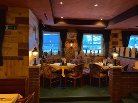 Ein gemütliches Restaurant mit Holzwänden und warmem Licht. Die Tische sind für Gäste vorbereitet und bieten eine einladende Atmosphäre.