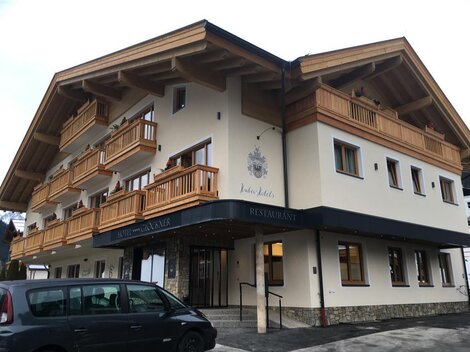 Ein modernes Gebäude mit mehreren Balkonen und einem Restaurant. Die Fassade ist in hellem Farbton gestaltet, umgeben von einem Parkplatz.
