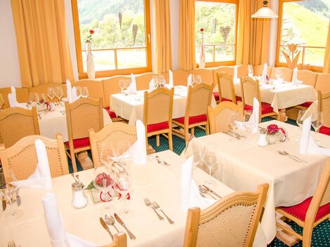 Ein eleganter Speisesaal mit gedeckten Tischen und festlicher Dekoration. Große Fenster bieten einen Blick auf die umliegende Landschaft.