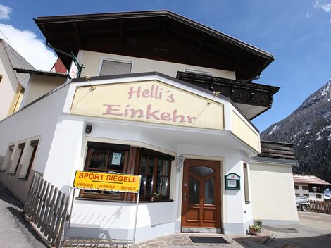 Ein gemütliches Gasthaus namens "Hell's Einkehr" in den Bergen. Die Fassade ist freundlich gestaltet und es gibt einen Blick auf die umliegenden Berge.