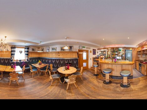 Eine gemütliche Bar mit Holzmöbeln und Tischen. Die Wände sind dekoriert und es gibt eine gut ausgestattete Bar im Hintergrund.