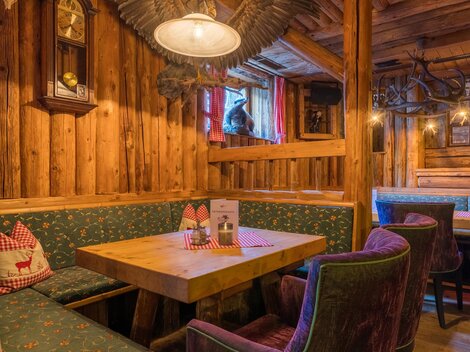 Eine gemütliche Stube mit Holzpaneelen und bequemen Sitzen. Auf dem Tisch stehen Menükarten und die Atmosphäre ist einladend.