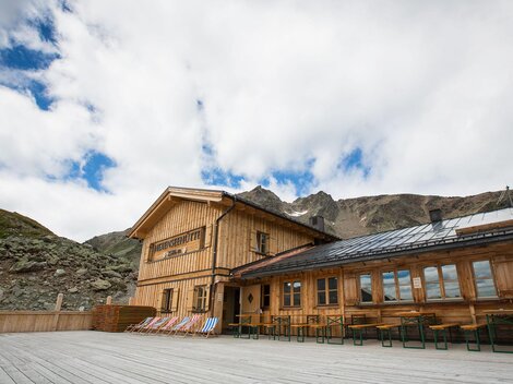 Ein rustikales Holzhaus in den Bergen mit großen Fenstern. Der Himmel ist bewölkt und die Umgebung ist natürlich und grün.
