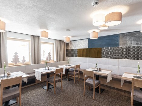 Ein modernes Restaurant mit hellen Wänden und stilvollen Lampen. Es gibt einfache Holztische und gemütliche Stühle, die eine einladende Atmosphäre schaffen.