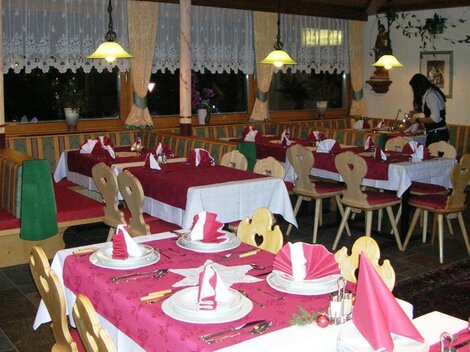 Ein einladendes Restaurant mit eleganten Tischen, die mit rotem Tischdecken und dekorativen Servietten gedeckt sind. Im Hintergrund ist eine Mitarbeiterin zu sehen, die den Service vorbereitet.