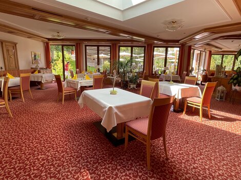 Ein einladendes Restaurant mit eleganten Tischen und roten Teppichboden. Große Fenster sorgen für viel Tageslicht und eine angenehme Atmosphäre.