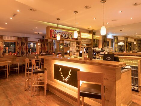 Eine einladende Bar mit Holzmöbeln und gedämpfter Beleuchtung. Im Hintergrund sind Theken und Regale mit Getränken zu sehen.