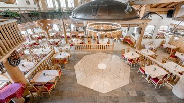 Ein einladendes Restaurant mit holzverkleideten Wänden und Tischen in Rot und Weiß. Große Fenster bieten viel Tageslicht und eine gemütliche Atmosphäre.