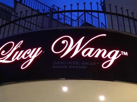 Ein Schild für das Hotel "Lucy Wang" mit einer eleganten Schriftart. Das Logo strahlt bei Nacht und zieht Aufmerksamkeit auf sich.