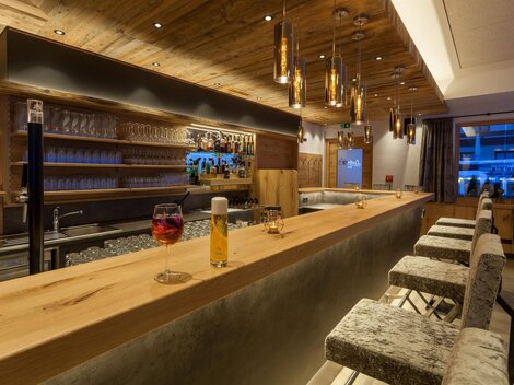 Eine moderne Bar mit Holzdekor und eleganten Leuchten. Im Hintergrund befinden sich Gläser und eine Auswahl an Getränken.