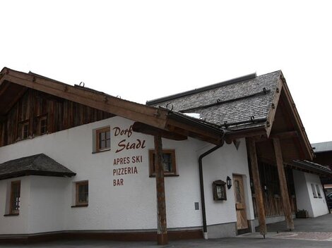 Ein gemütliches Restaurant mit Holzverkleidung, das für Après-Ski bekannt ist. Die Fassade zeigt den Namen "Dorf Stadl" und lädt zum Verweilen ein.