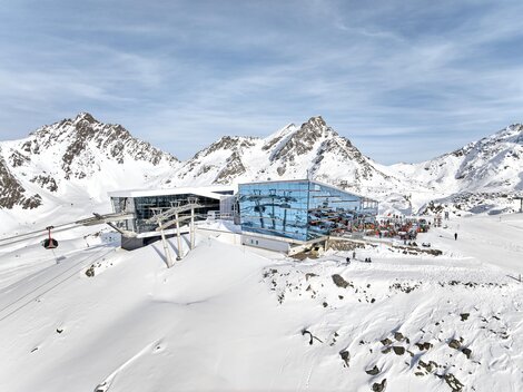 Eine moderne Bergstation in den verschneiten Alpen. Im Hintergrund sind majestätische Berge und ein klarer Himmel zu sehen.