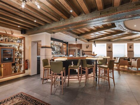 Eine elegante Bar mit Holzdecke und moderner Einrichtung. Gemütliche Sitze und ein gut bestücktes Regal verleihen der Atmosphäre einen einladenden Charakter.