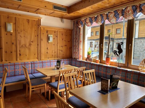 Ein gemütliches Restaurant mit Holzmöbeln und karierten Polstern. Große Fenster lassen viel Licht herein und bieten einen Blick nach draußen.