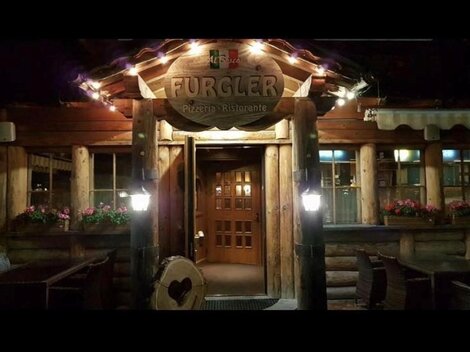 Ein rustikales Restaurant aus Holz mit einer einladenden Fassade und warmem Licht. Die Eingangstür ist aus Holz und die Fenster sind mit blühenden Pflanzen geschmückt.