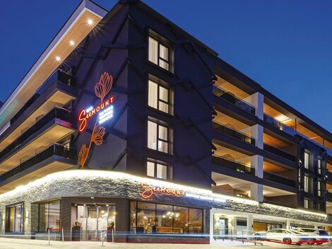 Ein modernes Hotelgebäude bei Nacht mit beleuchteter Fassade. Die Fenster reflektieren das stimmungsvolle Licht der Umgebung.