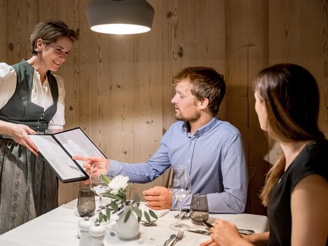 Eine Kellnerin serviert das Menü an ein Paar in einem gemütlichen Restaurant. Die warmen Holzwände schaffen eine einladende Atmosphäre.
