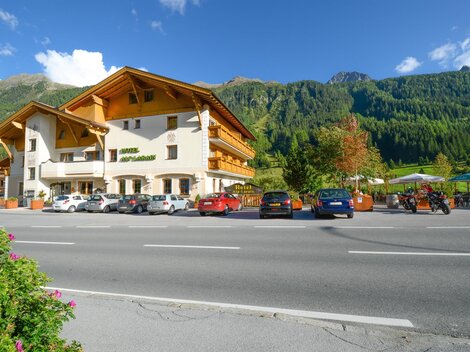 Ein hübsches Hotel mit traditioneller Architektur liegt am Straßenrand. Im Hintergrund sind grüne Berge und Bäume zu sehen.