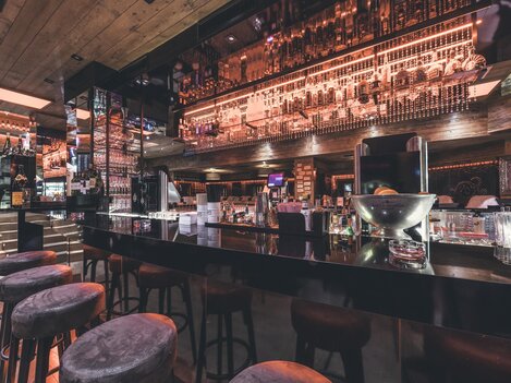 Eine moderne Bar mit einer eleganten Theke und stilvollen Barhockern. Die Beleuchtung und Dekoration schaffen eine einladende Atmosphäre.
