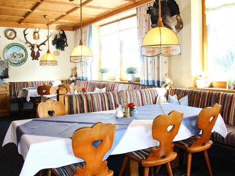Ein gemütliches Restaurant mit Holzmöbeln und bunten Sitzbänken. Der Raum ist hell und einladend, mit dekorativen Jagdtrophäen an den Wänden.