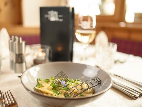 Ein stilvoll gedeckter Tisch mit einem Teller Pasta und frischem Gemüse. Im Hintergrund sind ein Getränk und eine Menükarte zu sehen.