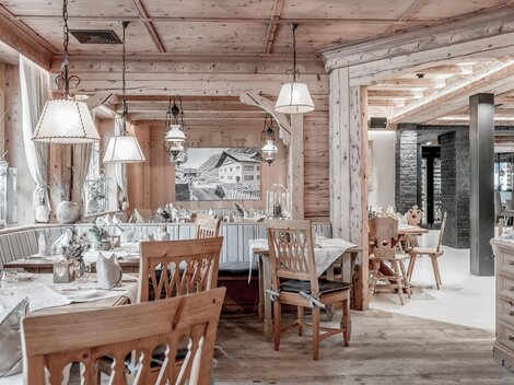 Ein gemütliches Restaurant mit Holzverkleidung und warmem Licht. Es sind Tische mit eleganten Tischdecken und Stühlen aus Holz eingedeckt.