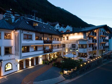 Ein charmantes Gebäude im alpenländischen Stil, beleuchtet in der Abenddämmerung. Umgeben von saftigen Bergen und einer einladenden Atmosphäre.