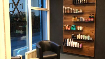Ein stilvolles Friseurstudio mit modernen Stühlen und einem Holzregal. Das Regal ist gefüllt mit verschiedenen Haarpflegeprodukten.